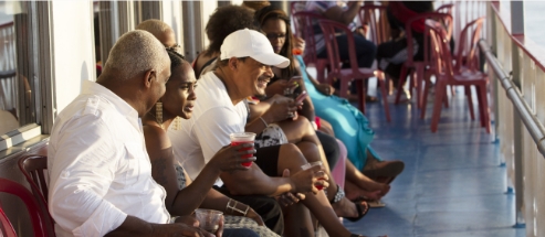 Group of people sitting in chairs on the riverboat deck with drinks in hand.